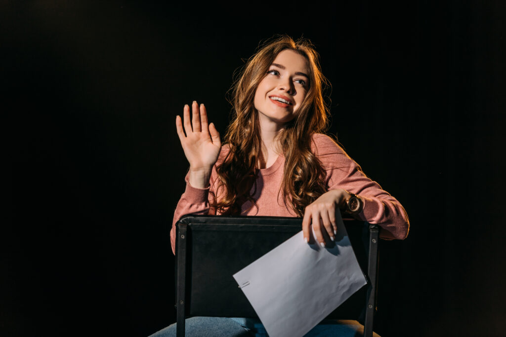 cheerful young actress with scenario sitting on chair on stage i